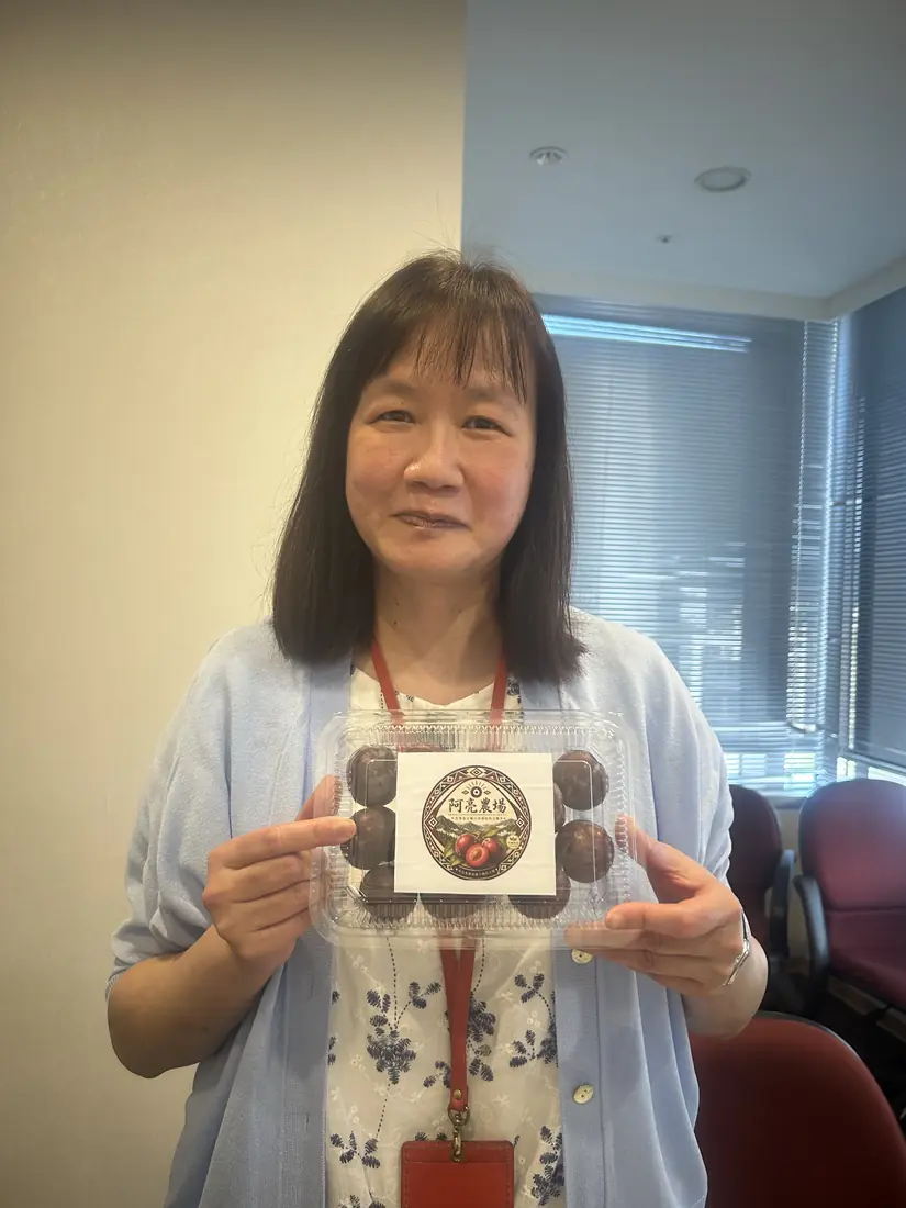 A friend who received red-flesh plums, smiling and holding a box with the Saluwan Farm label
